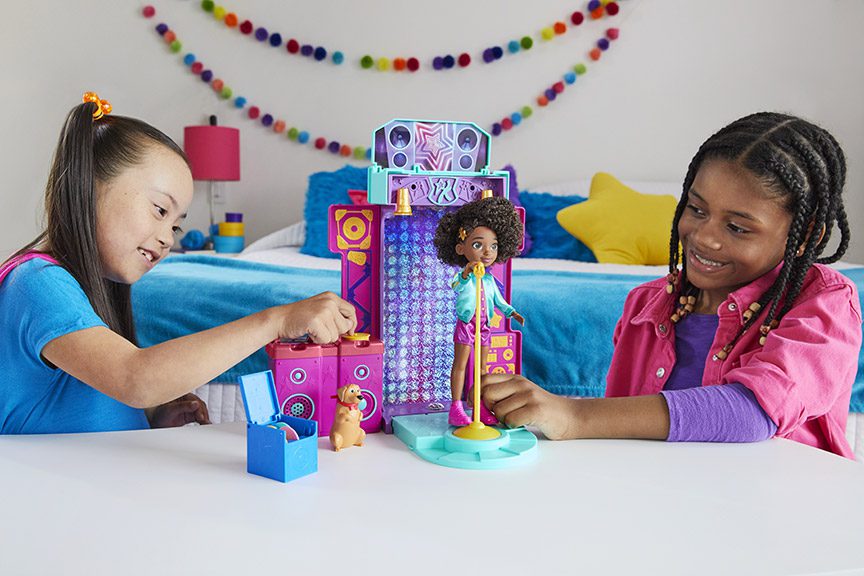 Two young girls playing with the Karma's World doll in their bedroom