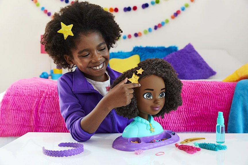 A young girl with a star barrette in her hair, adding a star barette into the hair of the Karma styling head toy