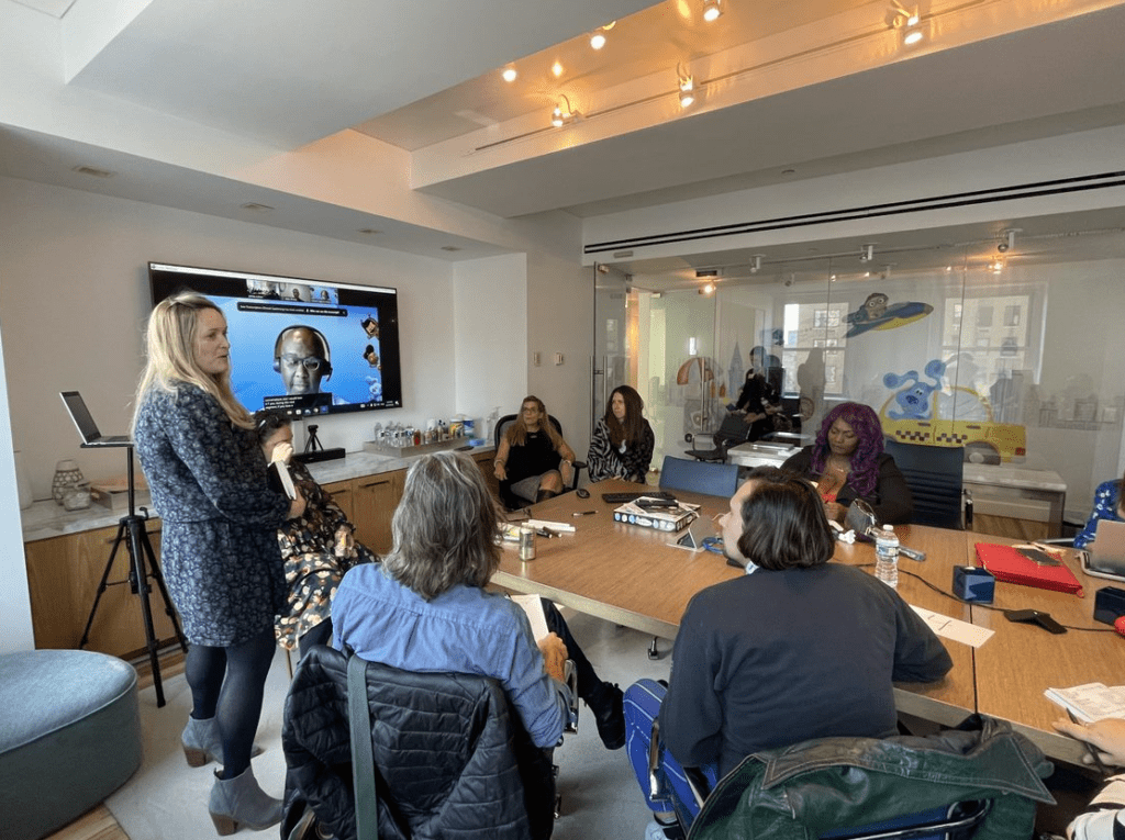 Danielle, a woman stands and presents in front of group of six Children's Content Lab event participants seated at desk. 