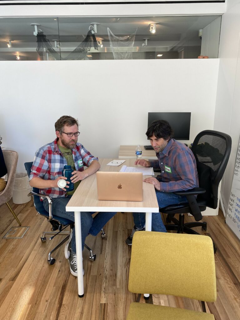 Two RespectAbility Lab fellows collaborate together at a desk over a laptop, while seated at a desk, in 9 Story's New York City studio.